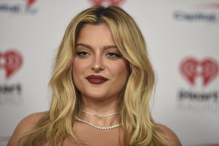 Bebe Rexha with long blond hair, red lipstick and diamond necklaces posing