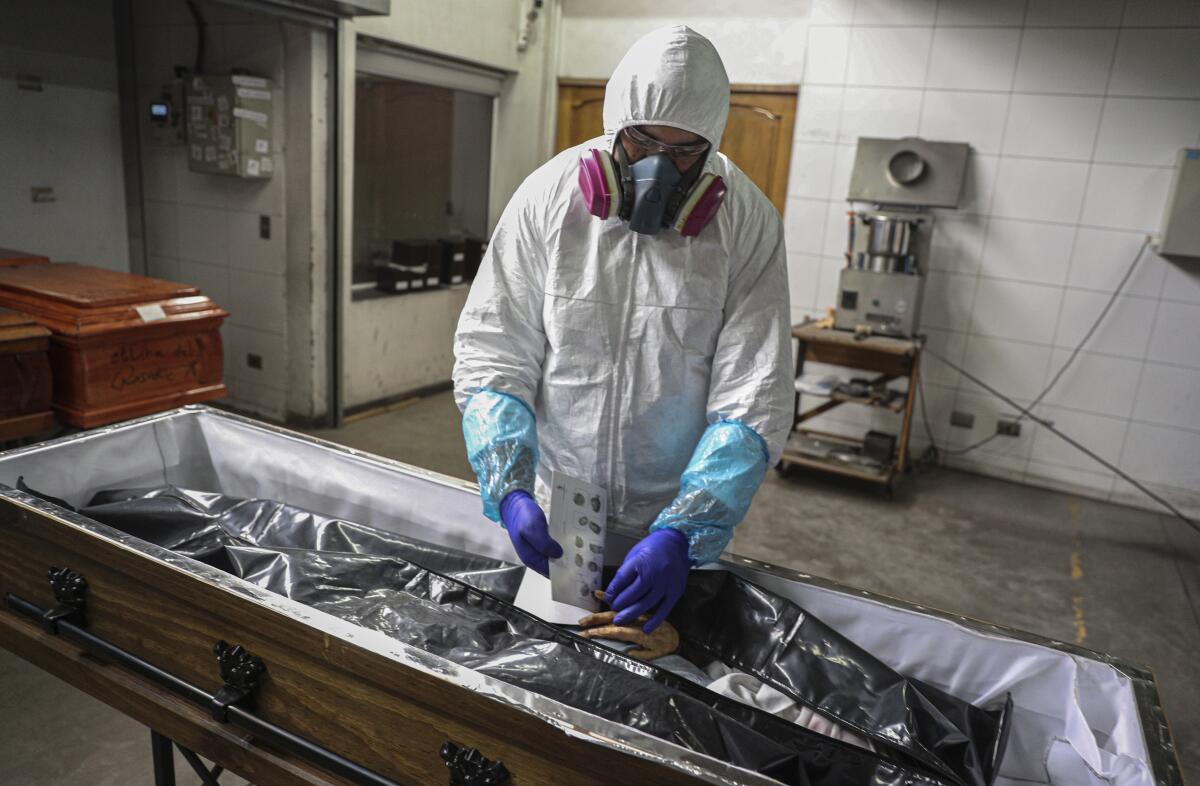A worker in protective gear takes fingerprints from a body in a casket.