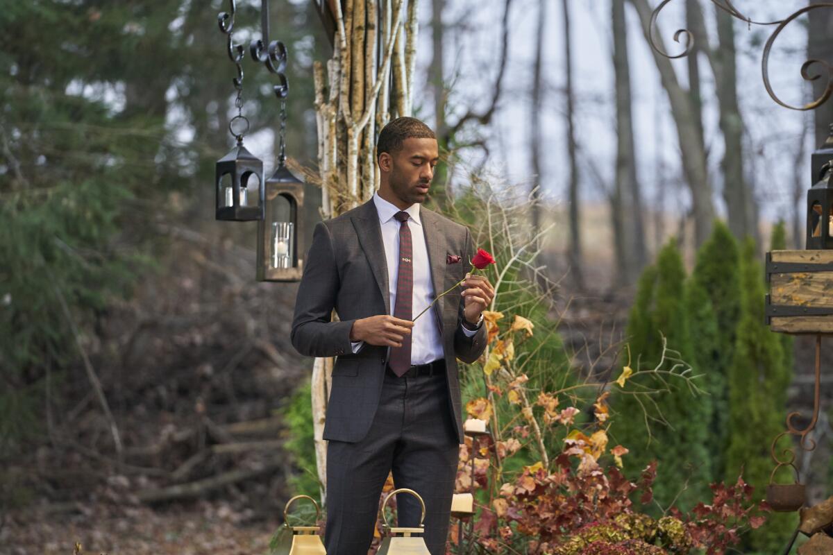 Matt James, the first Black lead in "Bachelor" history, standing with a rose amid fall foliage.