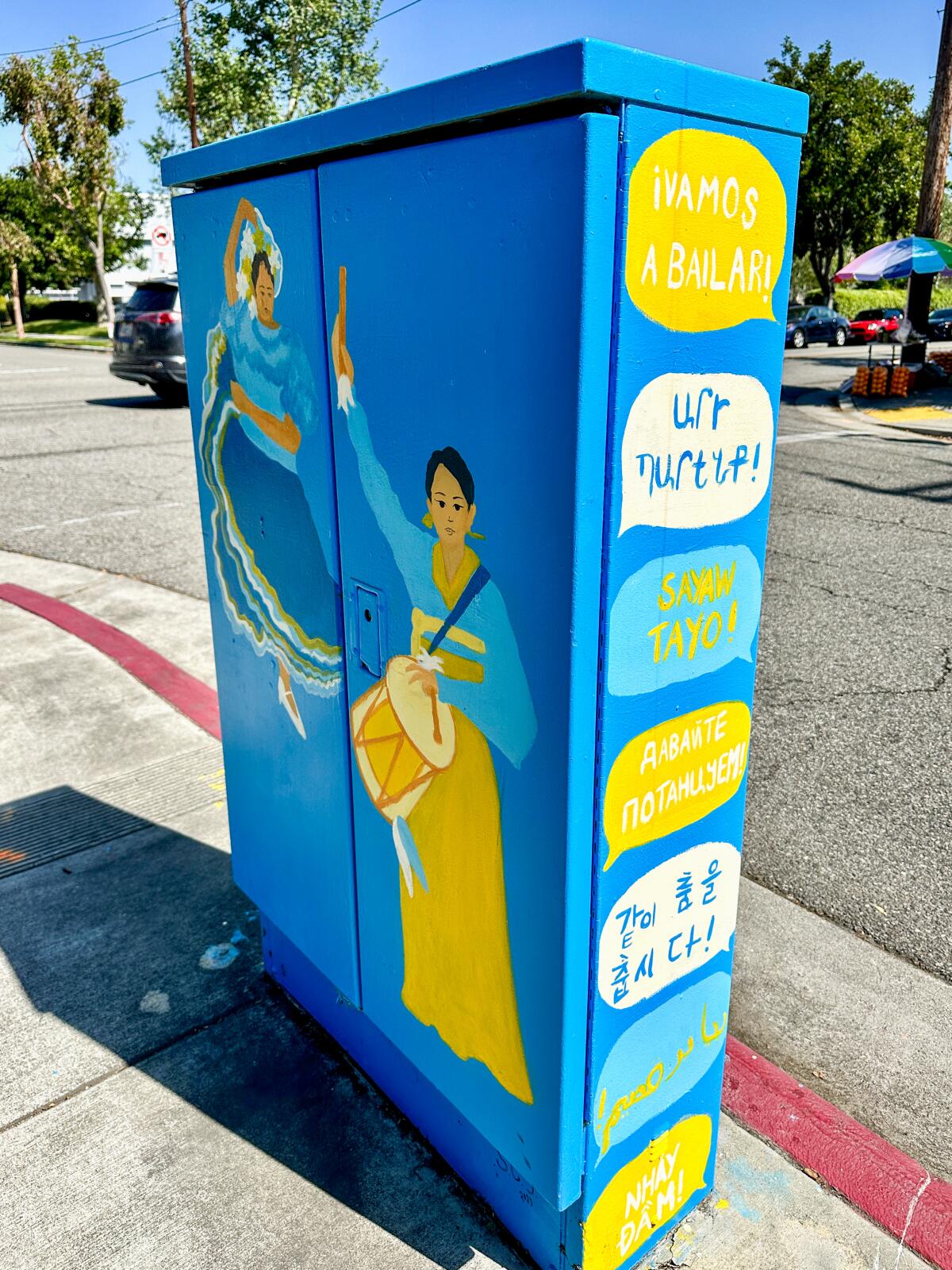 A utility box on a sidewalk is painted with invitations to dance in multiple languages.
