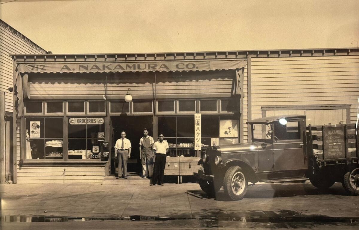 A historical photo shows three people standing outside the A. Nakamura grocery store on Terminal Island.