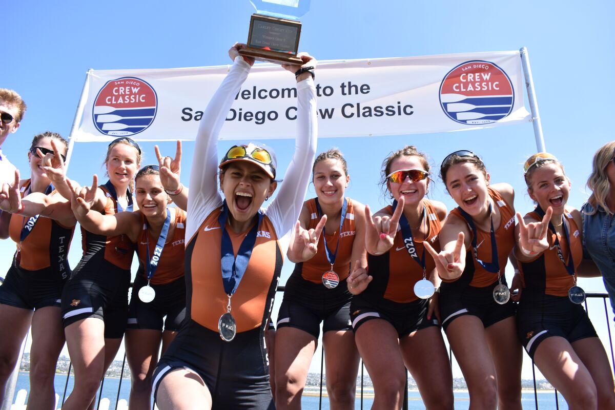 Eight rowers celebrate a win at the San Diego Crew Classic with one holding a trophy.