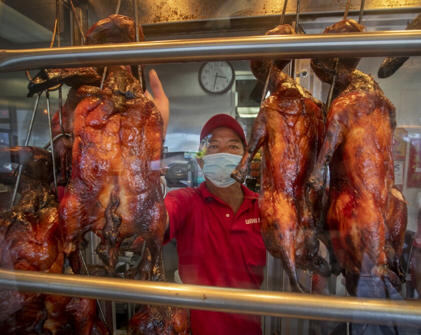 Vy Then wears a mask while selecting roast duck for a customer at Lien Hoa BBQ.