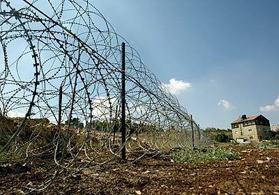 Several strands of concertina wire divide the land of a Palestinian household.