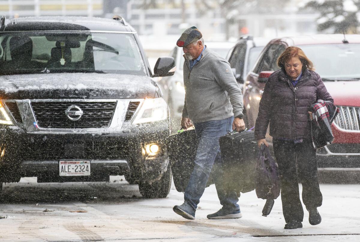 People carrying suitcases walk through snow in front of cars