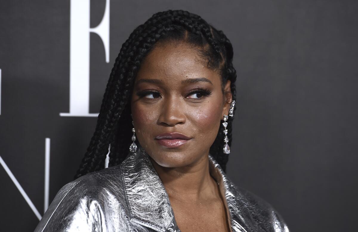 Keke Palmer looks to the side while posing in a silver jacket and dangly earrings.