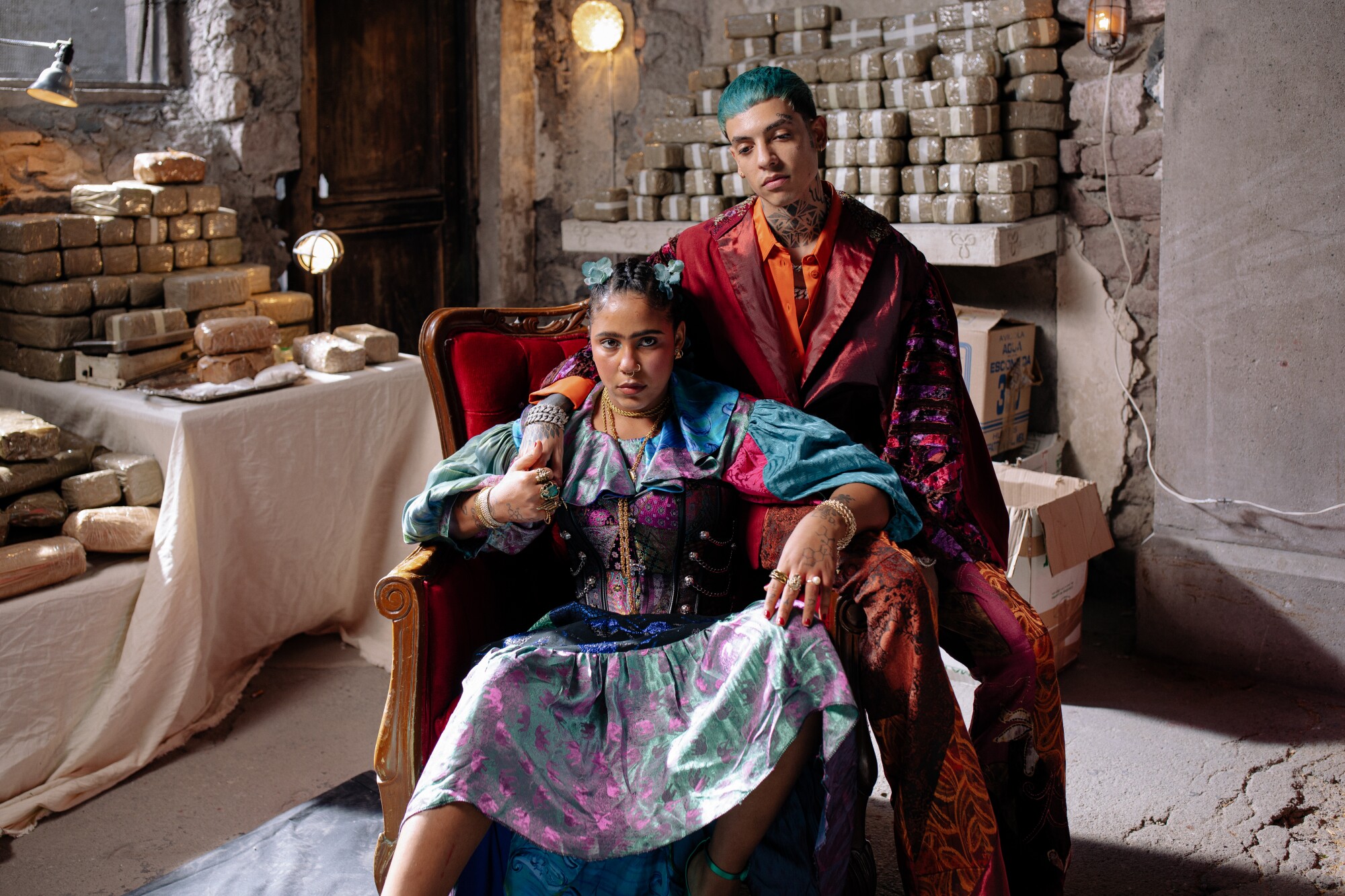 A woman, seated, and a man with blue hair behind her.