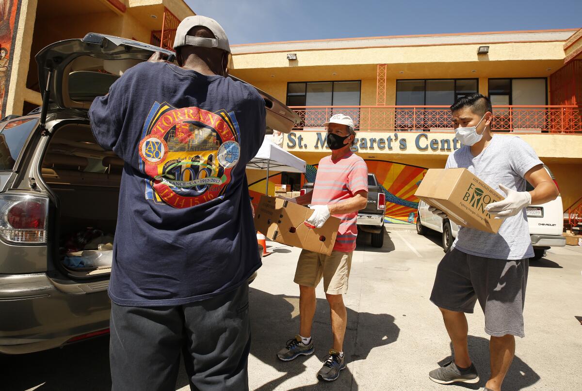 Roberto Calderon, left, and Ronson Chu, right, load a package of food at St. Margaret's Center Catholic Charities of Los Angeles as close to 300 families line up now each Wednesday to collect food at a drive-thru and walk-up pantry.