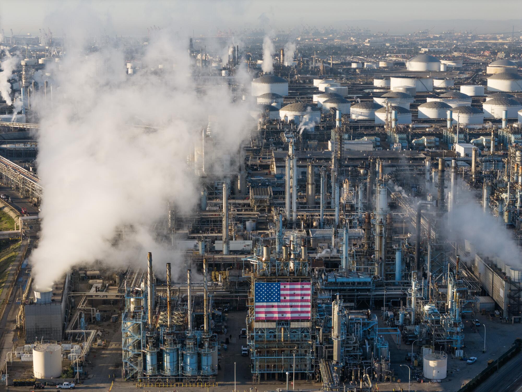 A view of refinery smokestacks, with a U.S. flag, and storage tanks in the background