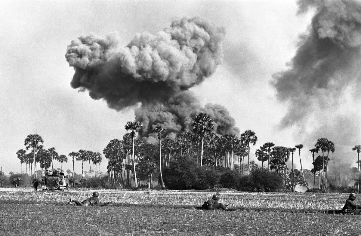 A mushrooming smoke cloud from air strikes on enemy positions serves as a backdrop for South Vietnamese Rangers who crouch behind paddy dike in foreground as armored personnel carriers advance near Cau Sap in Cambodia’s Parrot’s Beak area on May 7, 1970. (AP Photo/Nick Ut)