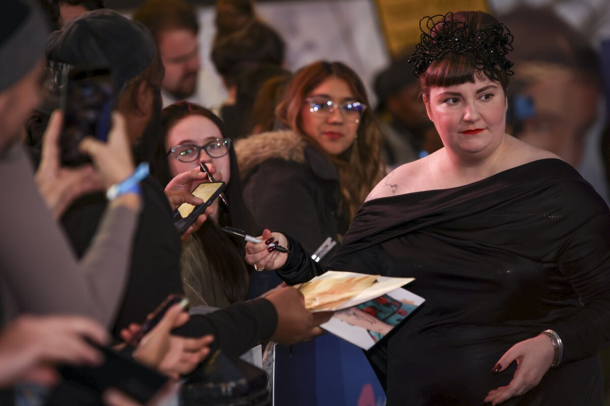 A  woman in a black gown signs autographs at a film premiere.
