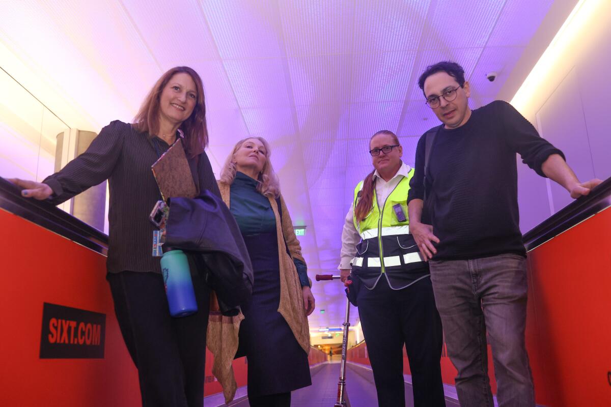 Four people walk along a moving sidewalk under a purple illuminated ceiling