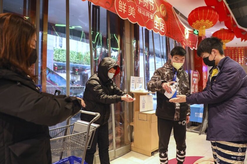 An employee distributes disinfectant to customers, all wearing surgical-style face masks, at the entrance to a supermarket in Wuhan, China, the epicenter of the coronavirus epidemic.