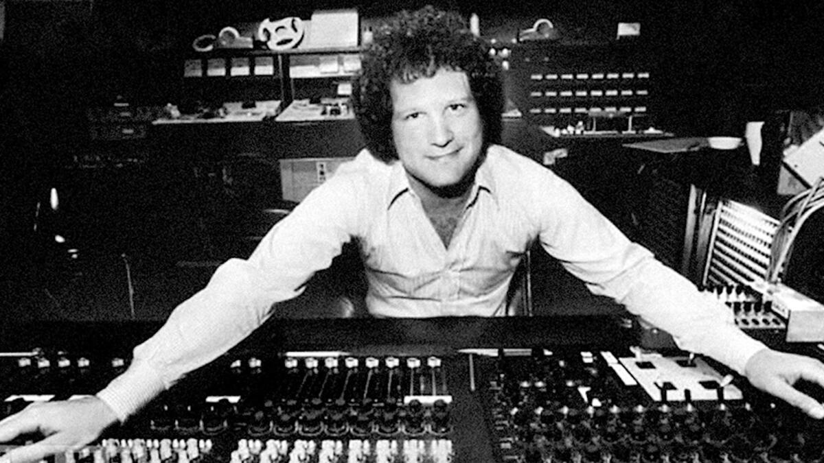 A black and white image of Albert Brooks posing over a sound control panel.