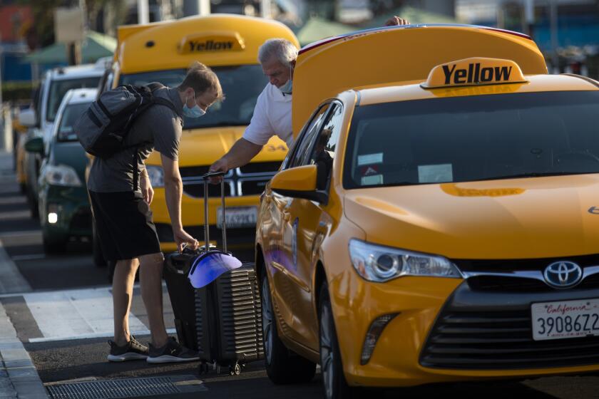 Los Angeles, CA. OCTOBER 18, 2020: A taxi driver helps a departing passenger with his luggage in line of tax's at LAX-it located east of Los Angeles International Airport in Los Angeles, CA Saturday afternoon October 18, 2020. (Francine Orr/ Los Angeles Times)