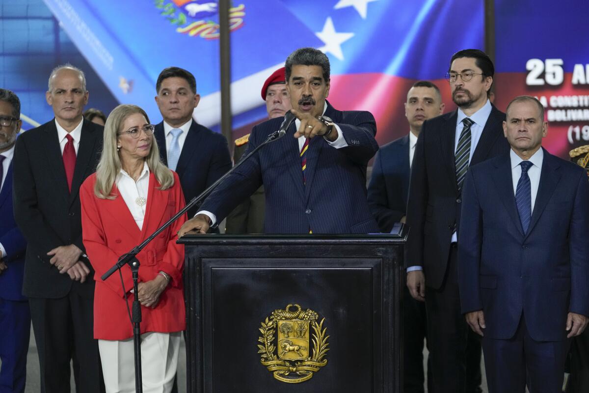 Venezuelan President Nicolás Maduro speaks to the press while several people stand behind and beside him.