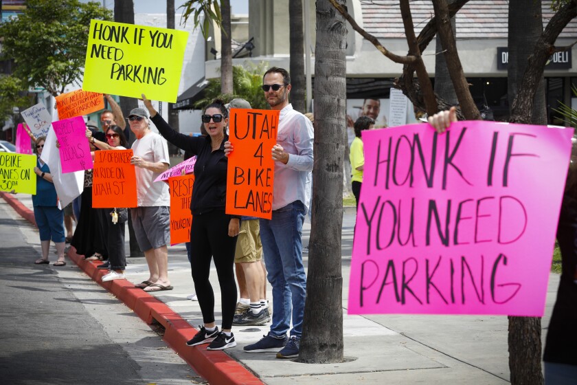 Protestors along 30th Street in North Park hold signs saying "Honk if you need parking"  along red-painted  curbs