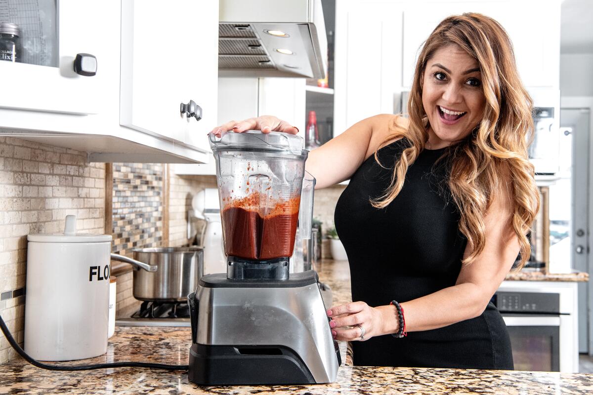 A smiling woman is about to start a blender in her kitchen