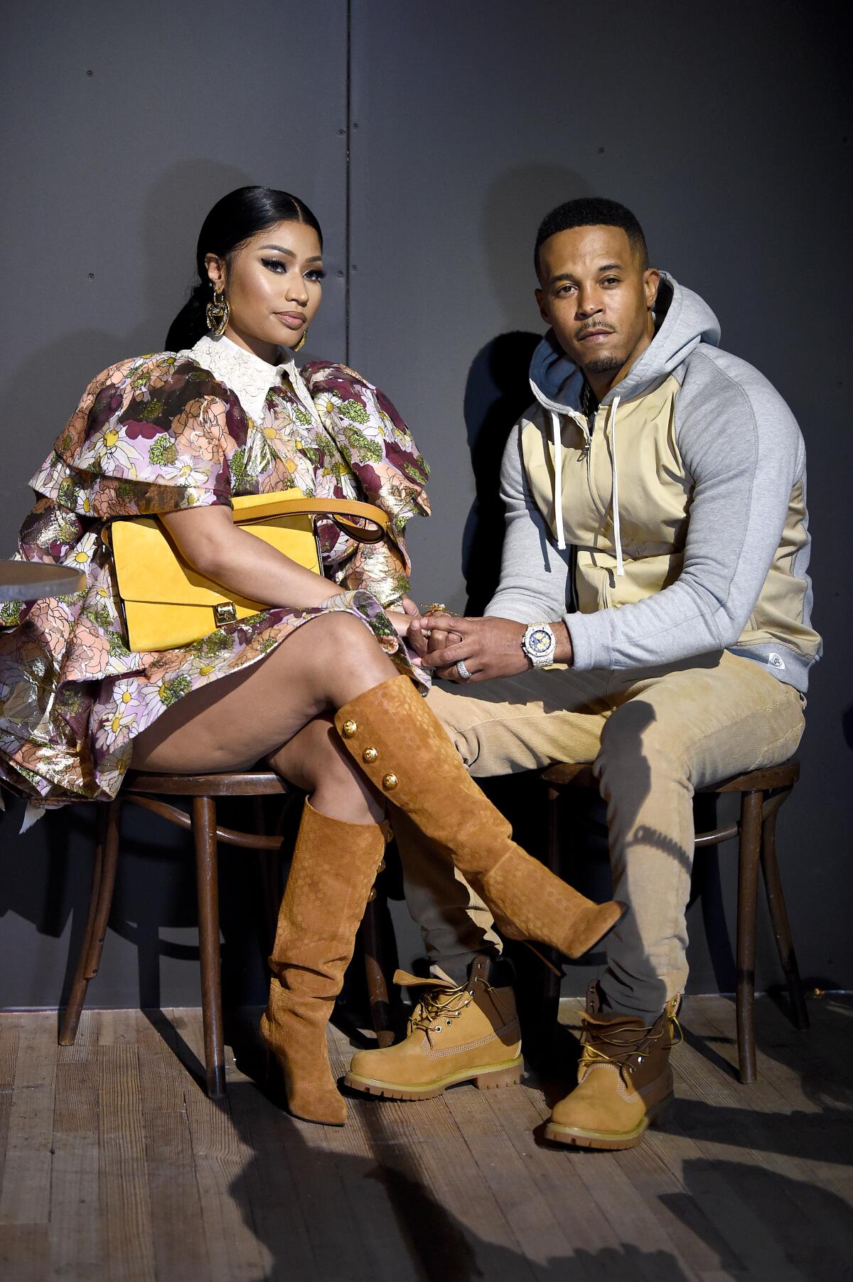 A woman and man hold hands while sitting on wooden chairs