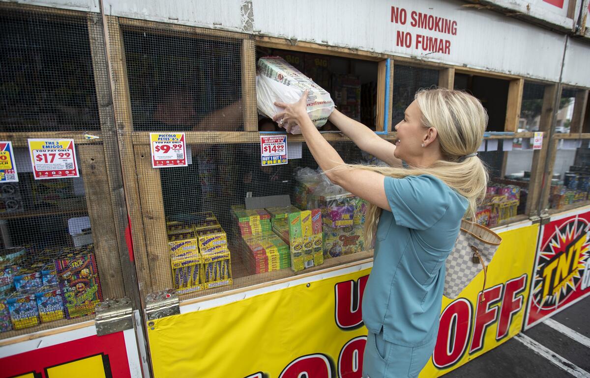 Elizabeth Geyer is handed her fireworks at the Costa Mesa High School Cheer team fireworks stand in Costa Mesa on Wednesday.