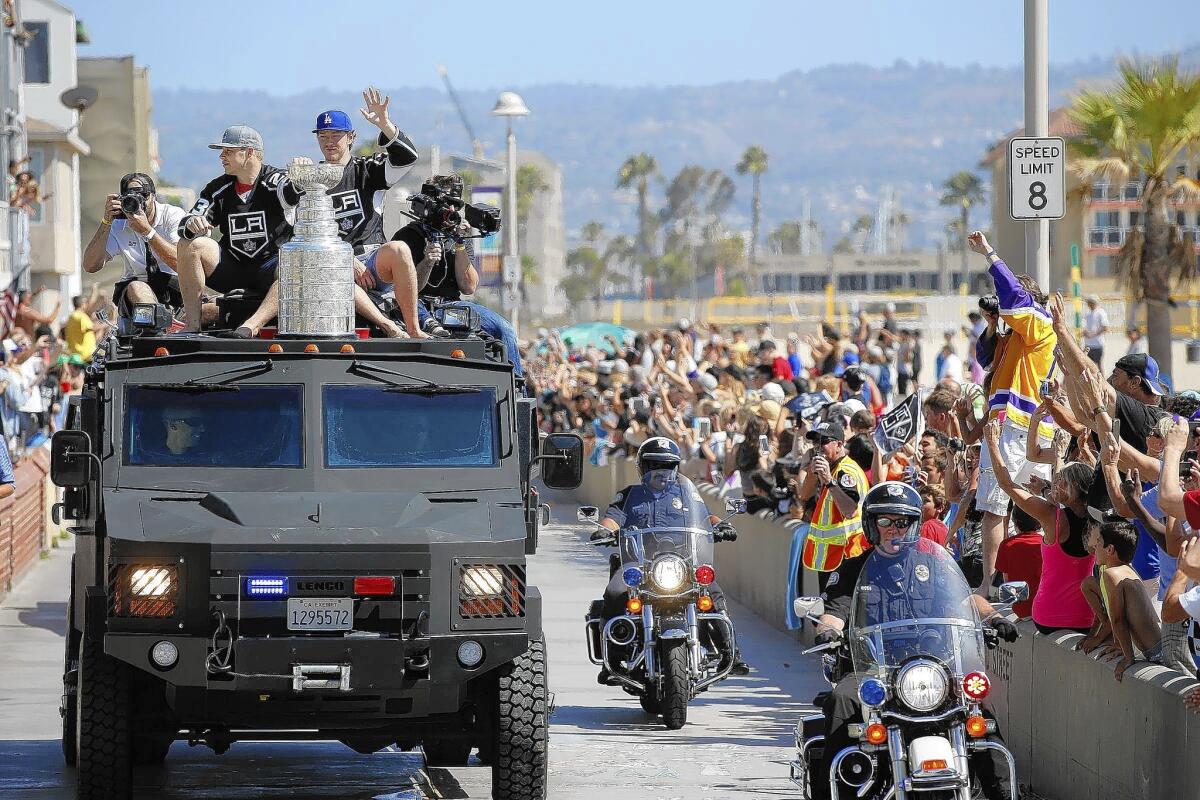 Riding on an armored police vehicle, Kings players Dustin Brown, left, and Tyler Toffoli hold onto the Stanley Cup as the team parades along the Strand in Hermosa Beach.