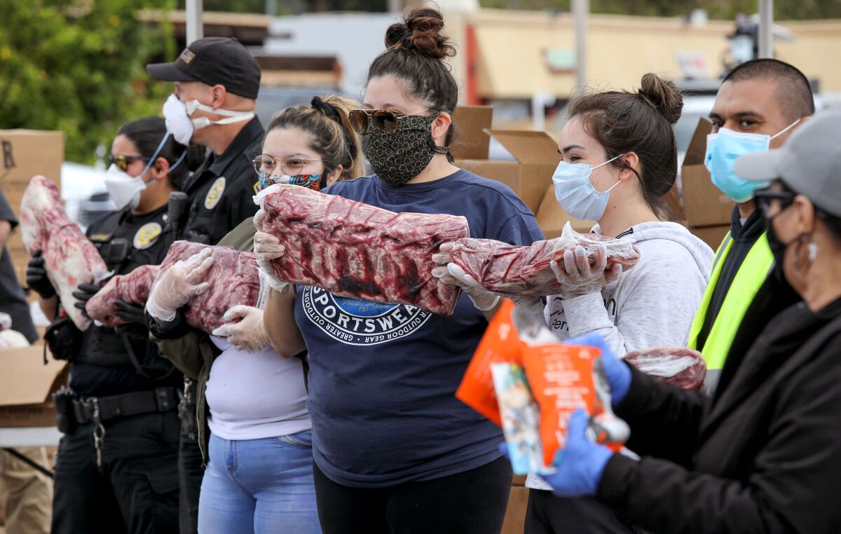 Volunteers and Escondido police officers form a line to give away large packages of meat and beef jerky to lines of vehicles passing through the parking lot of Kennedy's Meat Company on Saturday.