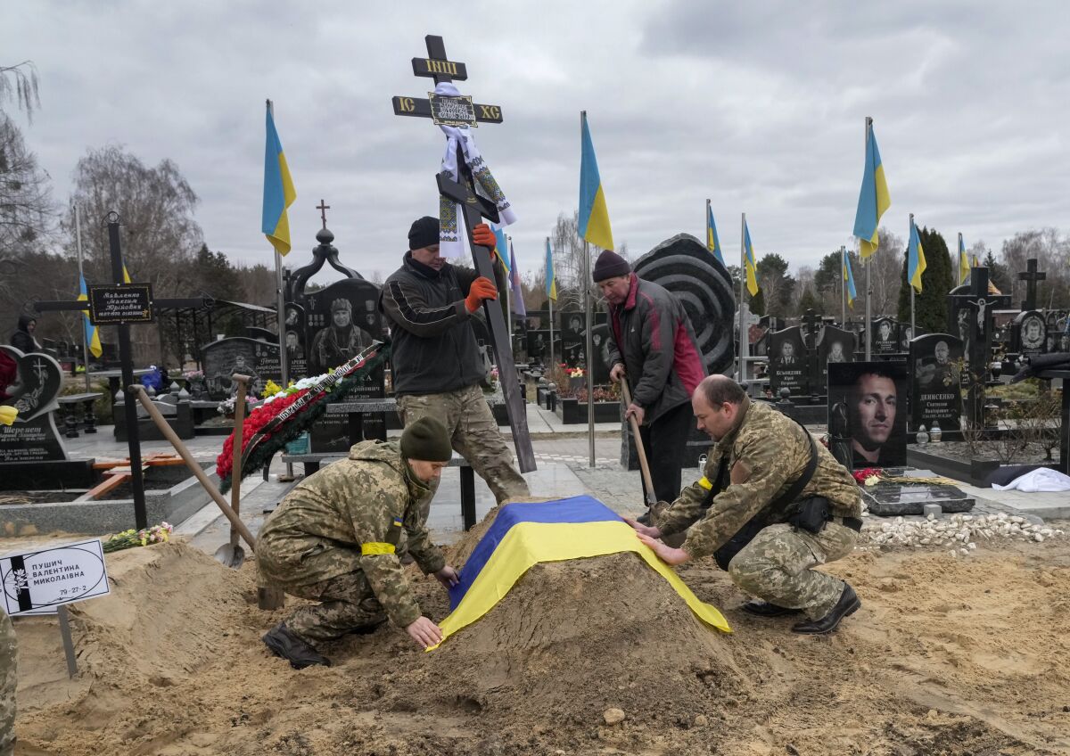 Ukrainian paramedics cover with the National flag the grave of their colleague Valentyna Pushych killed by Russian troops in a cemetery in Kyiv, Ukraine, Saturday, March 5, 2022. (AP Photo/Efrem Lukatsky)
