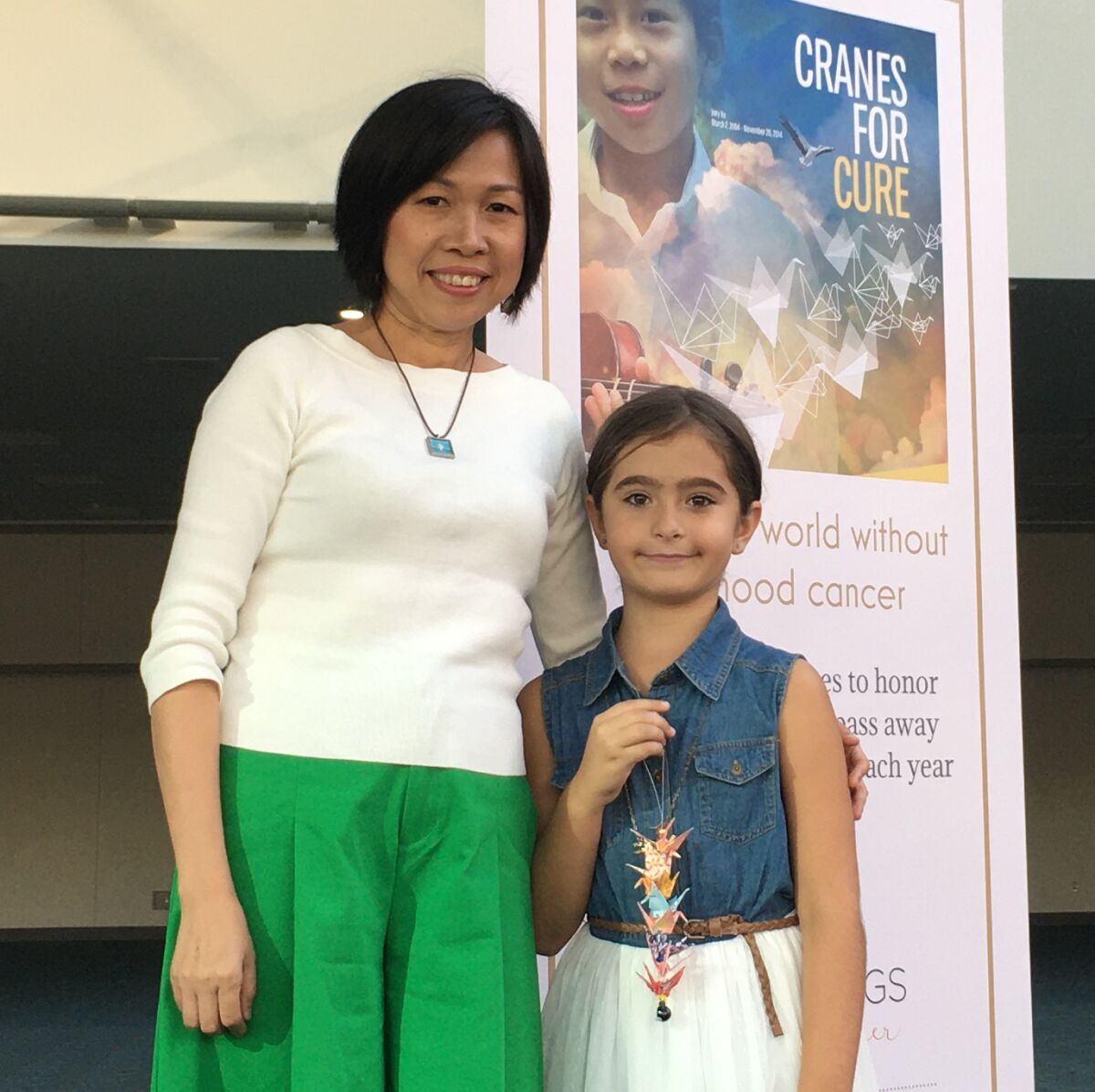 Barnard third-grade teacher Kathy Liu and student India Z. pose beneath the ‘Cranes for a Cure’ Pediatric Cancer Awareness art installation at San Diego Convention Center.