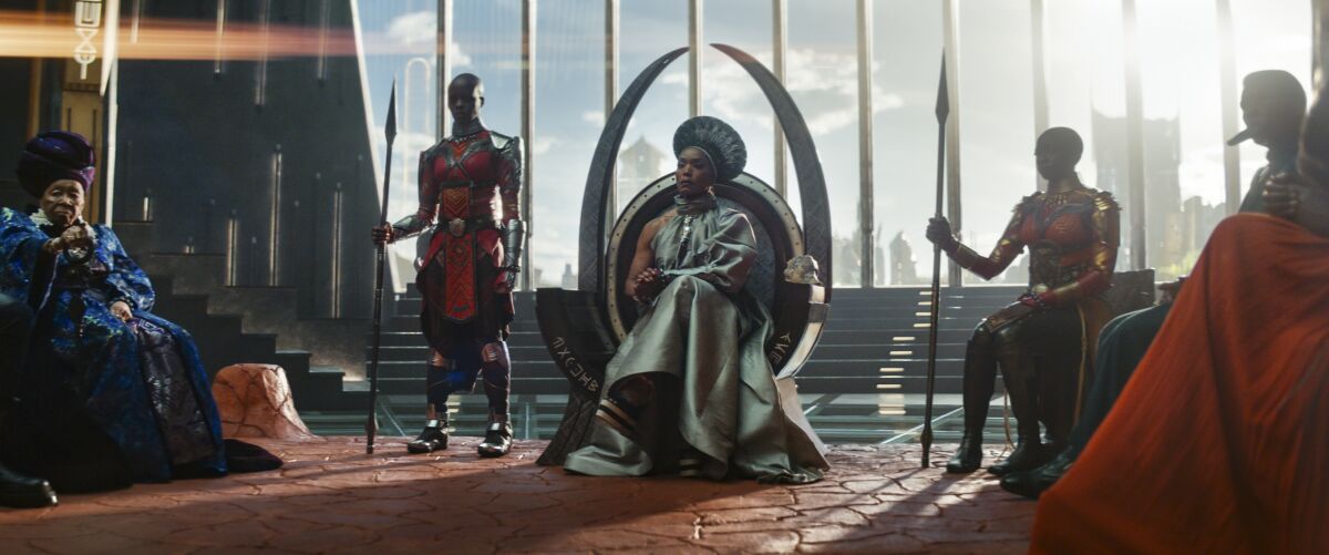 A woman sits on a futuristic throne flanked by guards in a scene from "Black Panther: Wakanda Forever."
