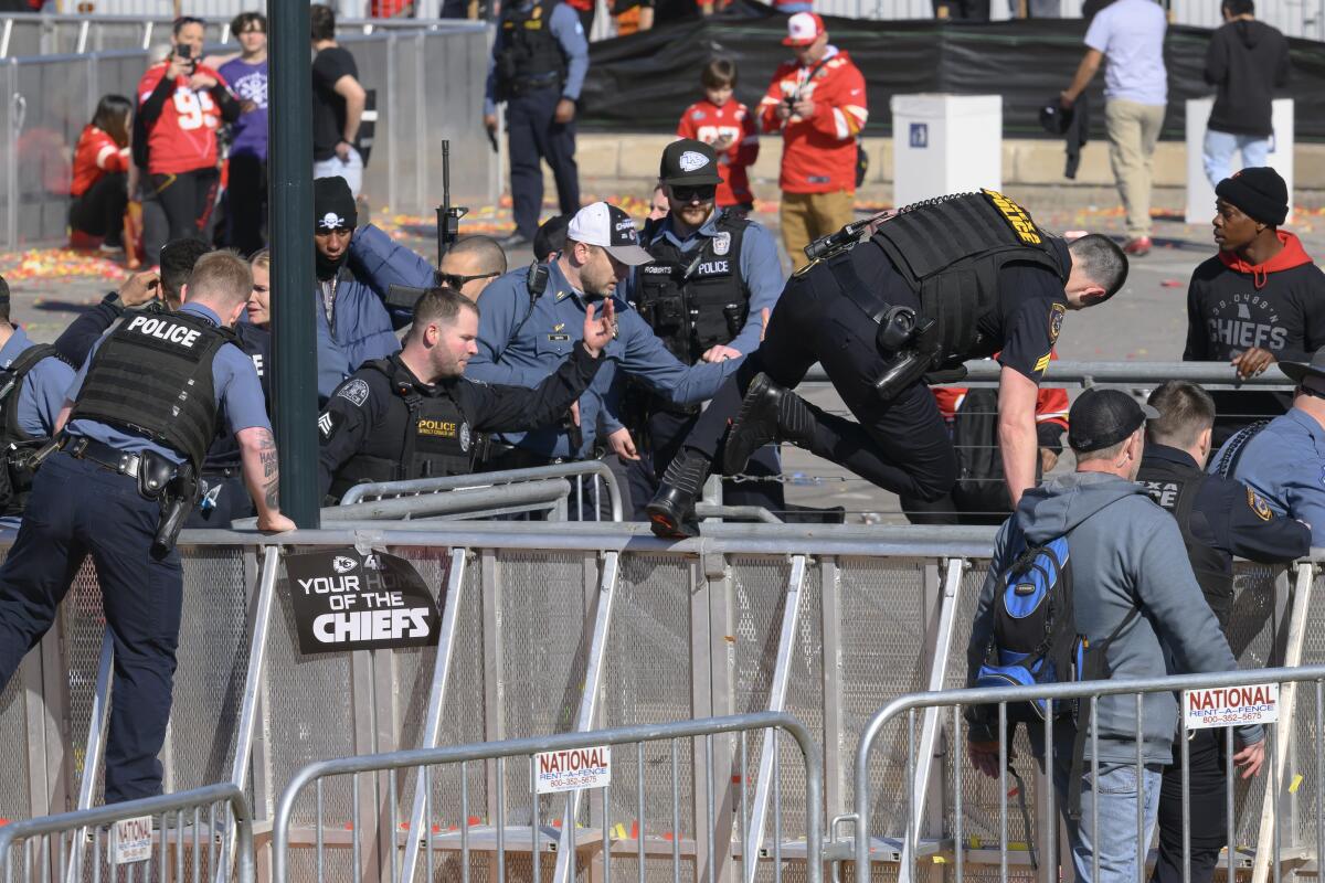 Police officers in dark uniform scramble over barricades as people stand in the background