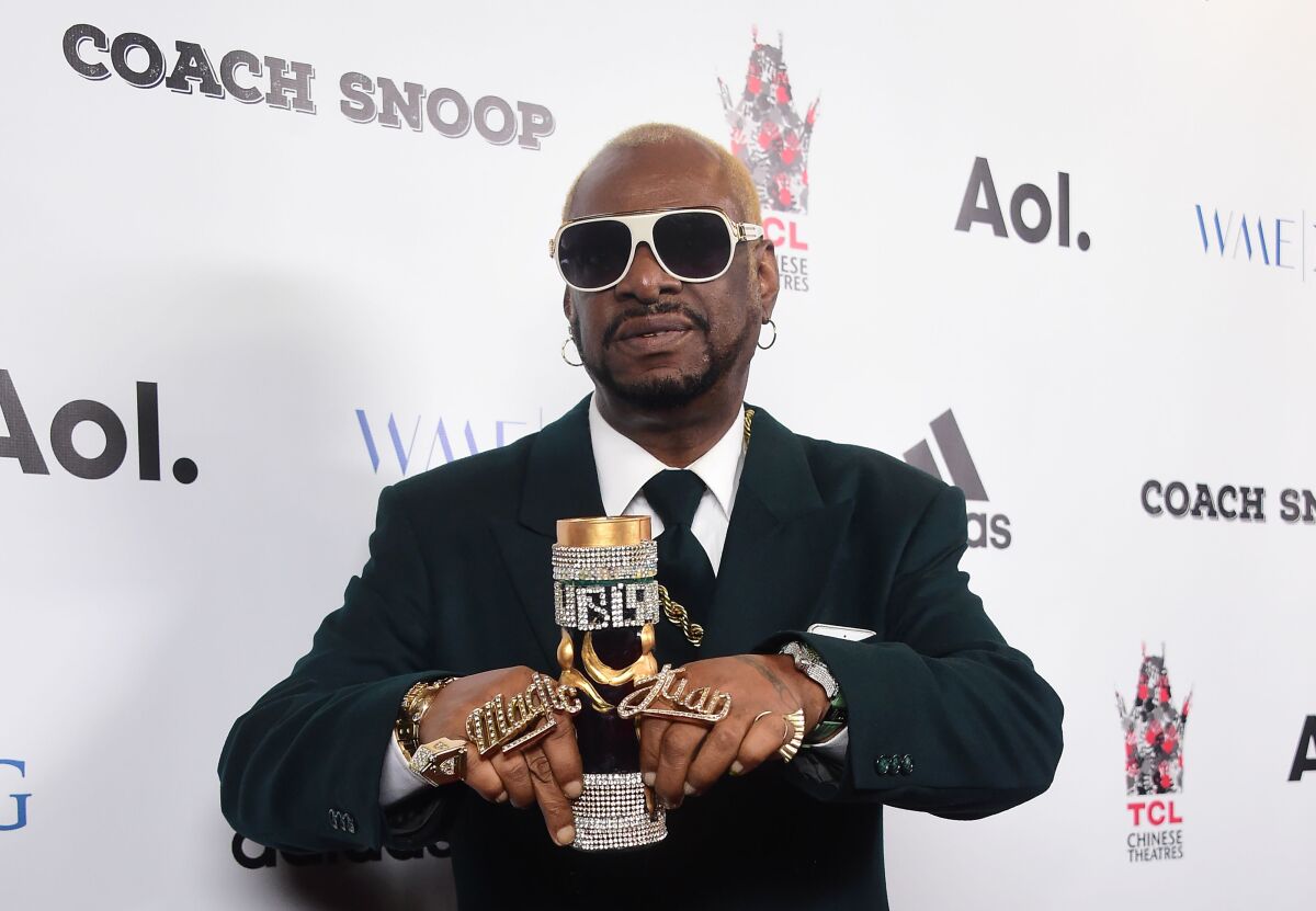 A man in sunglasses and flashy rings holds a blinged-out chalice at an event