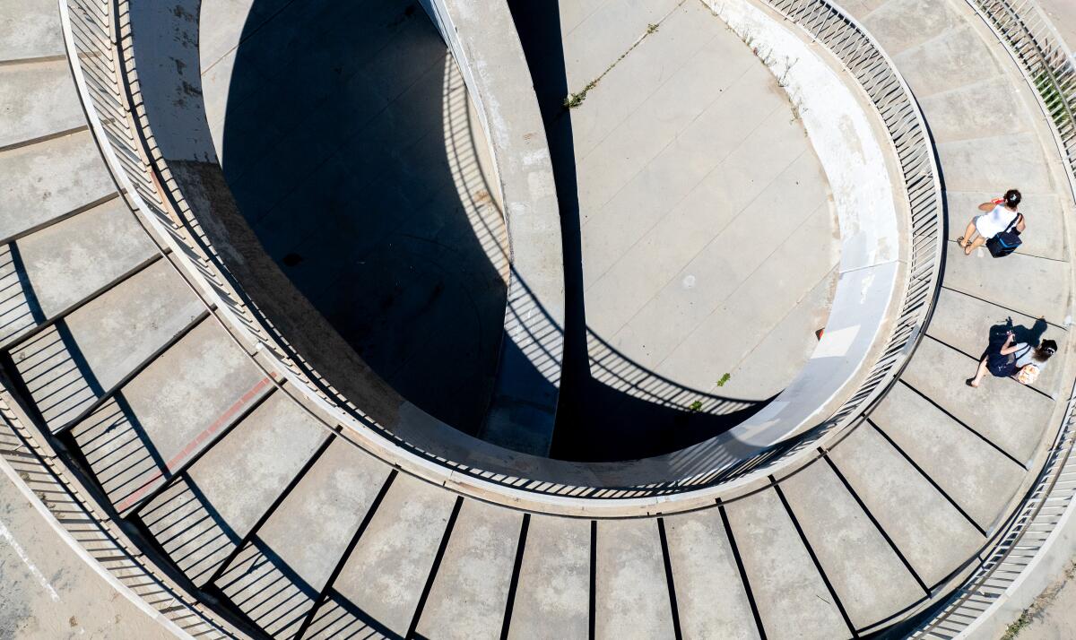 Beachgoers walk down a concrete spiral staircase across Pacific Coast Highway in Santa Monica