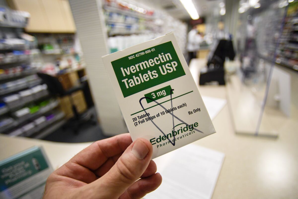 A box of ivermectin is shown in a pharmacy as pharmacists work in the background.