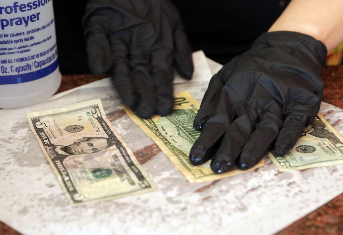 Maricela Moreno, a cashier at El Tarasco in Marina del Rey, dries the disinfected dead presidents on a paper towel before returning them to the cash drawer.
