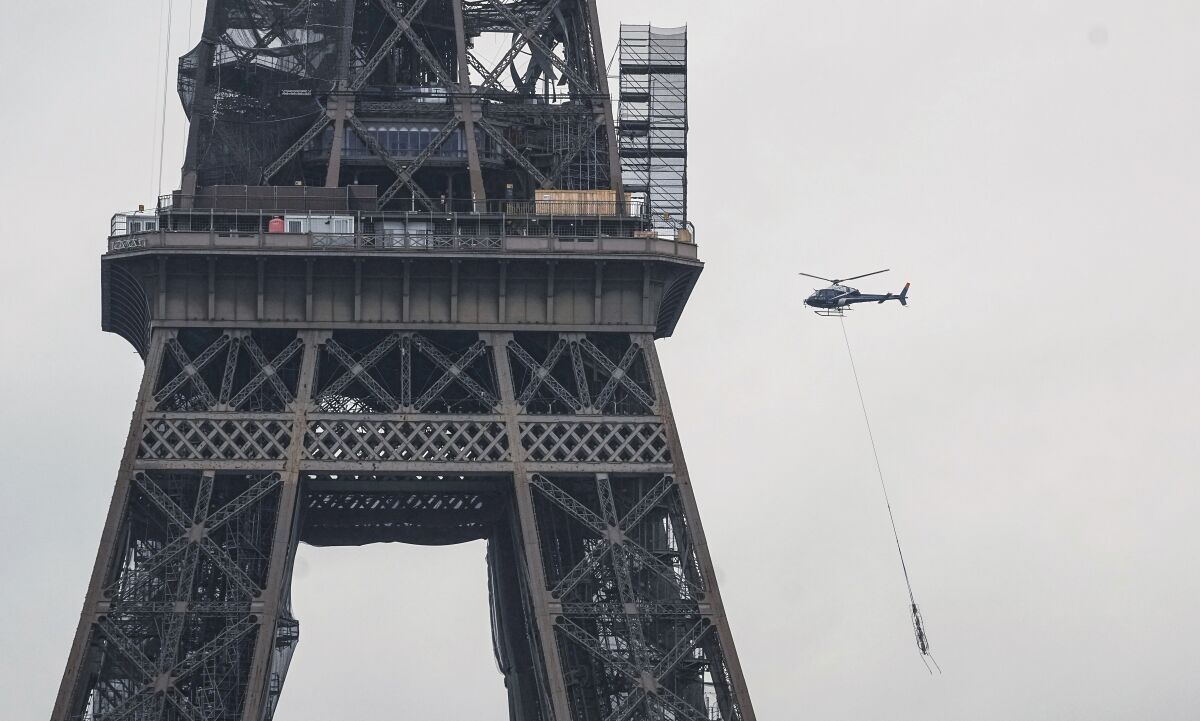 A new telecom transmission TDF (TeleDiffusion de France) antenna hanging from an Eurocopter Ecureuil 2 helicopter as the crew flies to install it on the top of the Eiffel Tower in Paris, Tuesday, March 15, 2022. The six meters antenna is raising the Eiffel Tower from 324 meters to 330 meters. (AP Photo/Michel Euler)