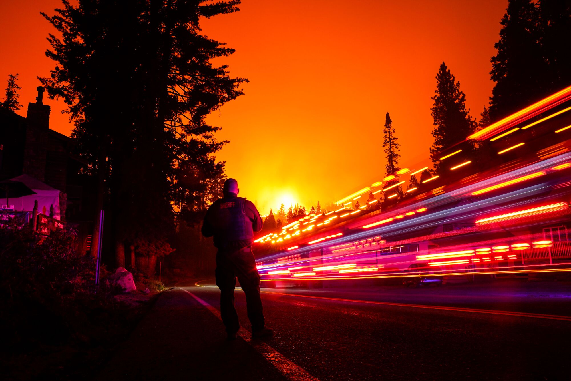 A man stands on the shoulder of a road as a vehicle streaks by in a long exposure. 
