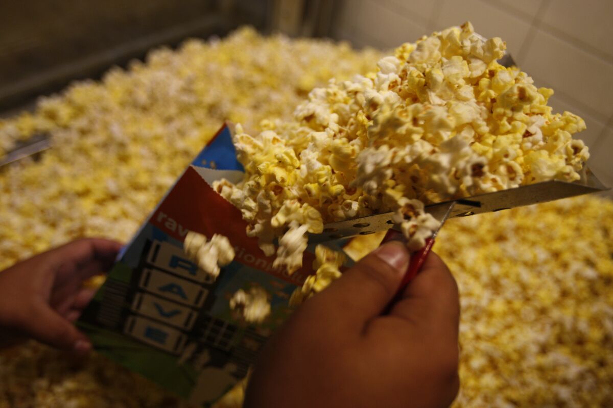 hands scoop popcorn into a paper bag 