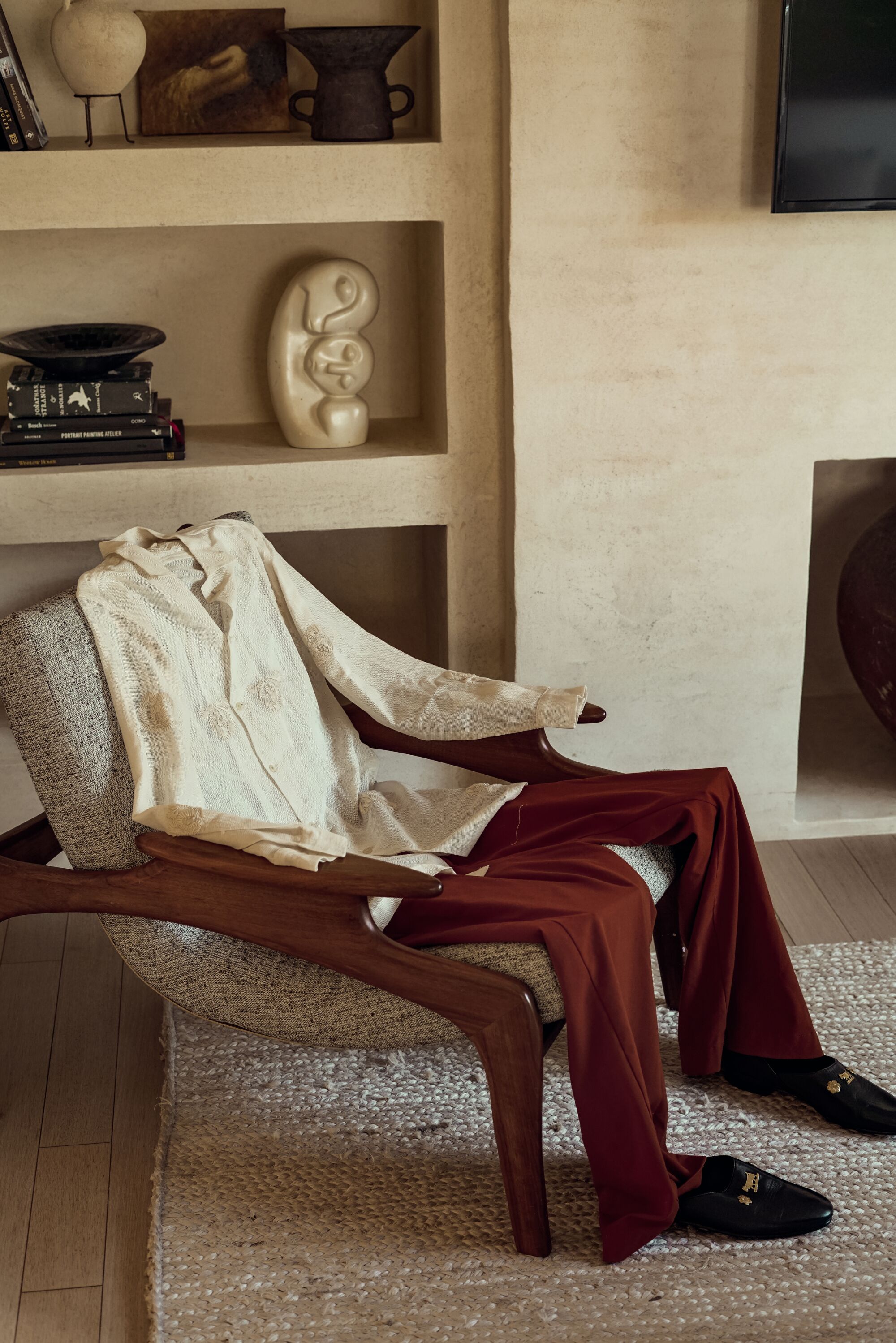 Bode Appenzeller house shoes and Bode Savoy Ribbon long sleeve tunic sit in a chair as if being worn by a human.