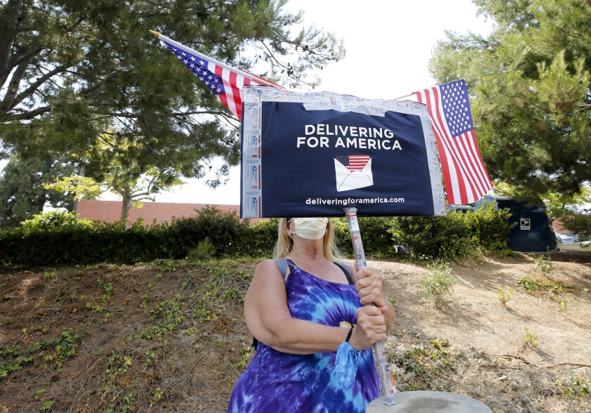 Valerie Honn holds a "Delivering for America" sign at a Save the USPS in Newport Beach.