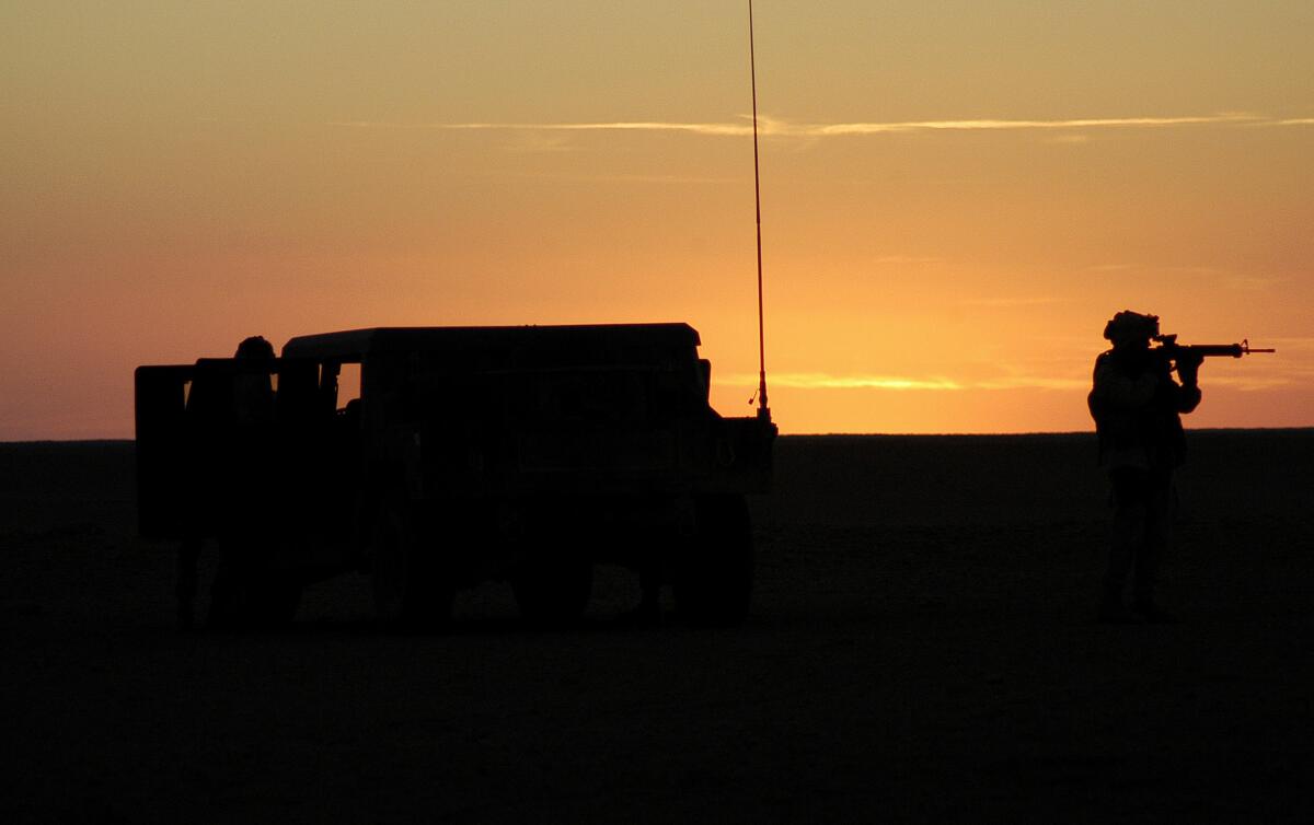 A silhouette of soldiers and their armored car against the desert at sunset