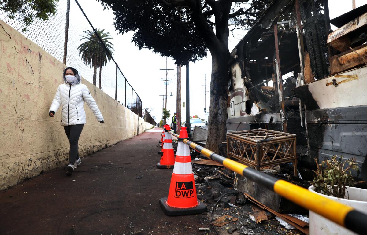 A pedestrian walking past a burned RV and traffic cones labeled "L.A. D.W.P."