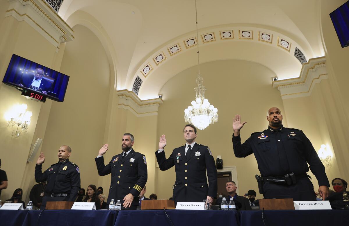 Police officers in uniform, rights hands raised in congressional hearing room