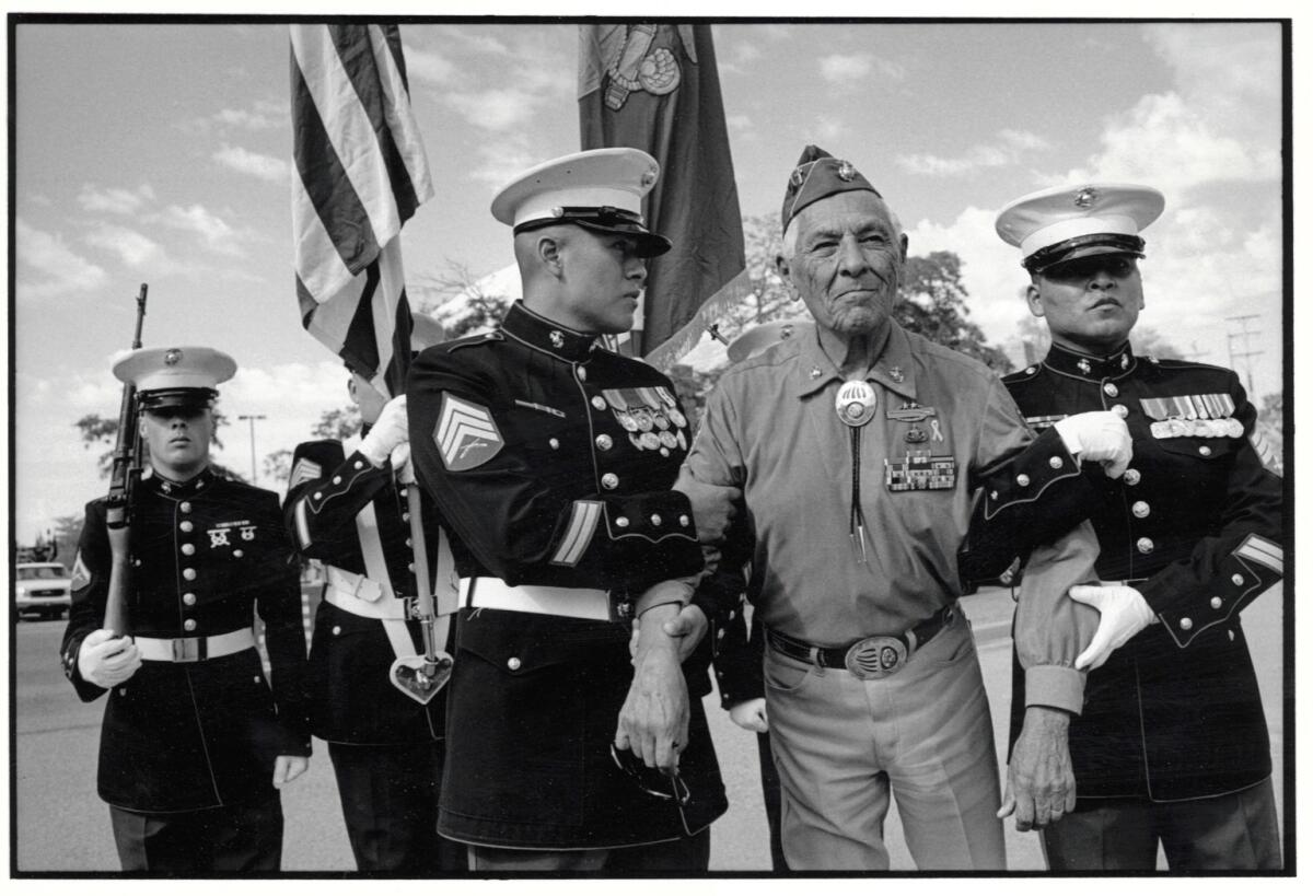 Two soldiers have their arms around another man who is wearing a cap.