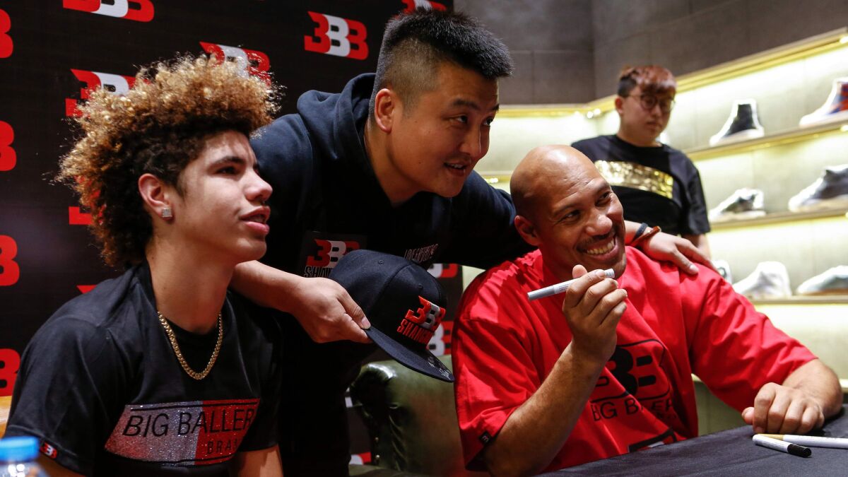 A basketball fan in Shanghai takes a photo with LaVar Ball, right, and LaMelo Ball, left, during a Big Baller Brand promotional event on Friday.