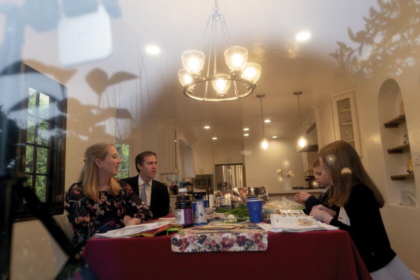 LOS ANGELES, CA - APRIL 08: During the coronavirus pandemic a view through the window of Passover Seder at Rabbi Nicole Guzik's and Rabbi Erez Sherman's home of Sinai Temple in LA on Wednesday, April 8, 2020 in Los Angeles, CA. Their family Rabbi Nicole Guzik, (left-right) Rabbi Erez Sherman, Annie Sherman, 8, and Zachary Sherman, 6, are at the table together. Their youngest son Henry Sherman, 4, fell asleep. They expect 100-200 people to join in through a Zoom link.