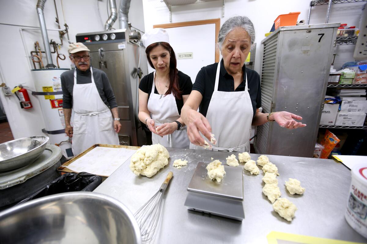 The Cakery Bakery previous owner Zora Yasseri, right, shows new owner Marjan Fadaei, center, what weight scones should be, at the bakery on Foothill Boulevard in La Cañada Flintridge on Tuesday. Previous owner Ray Yasseri looks on at left.