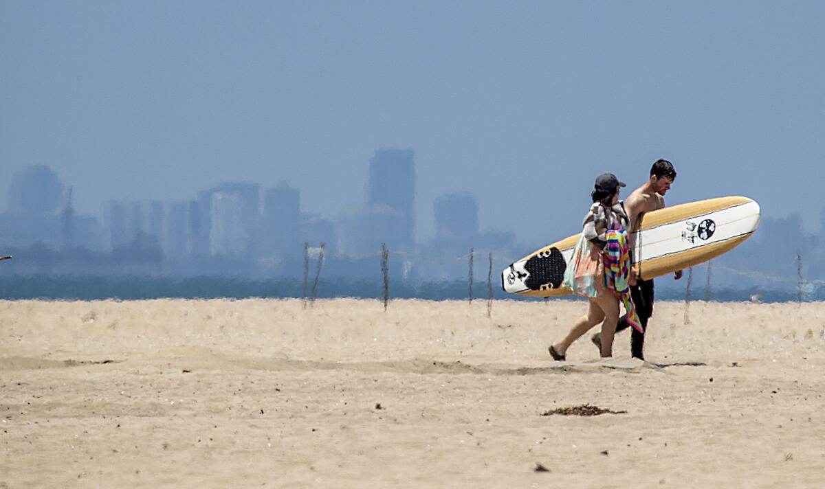 Beach goers return from surfing with a view of downtown Long Beach in the background before the Memorial Day weekend