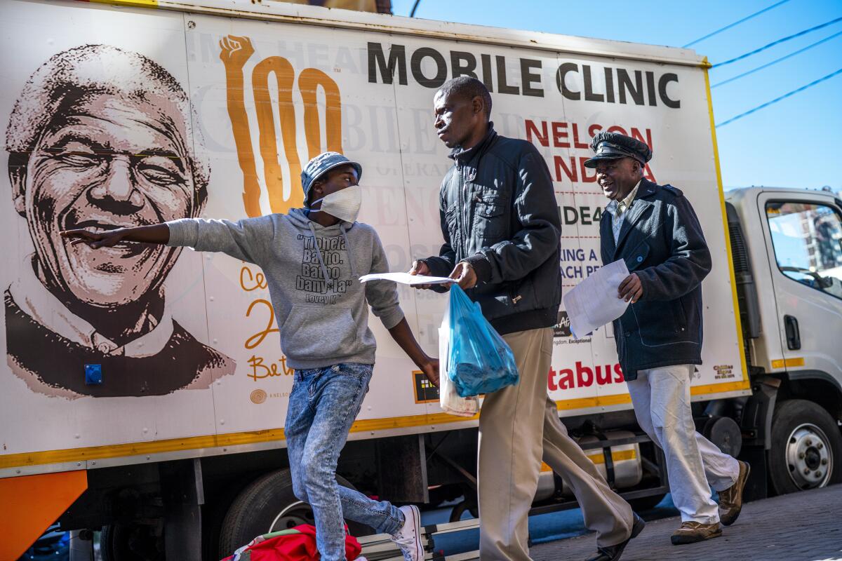 One man gestures to direct two others in front of a truck with Nelson Mandela's image that says "Mobile Clinic"