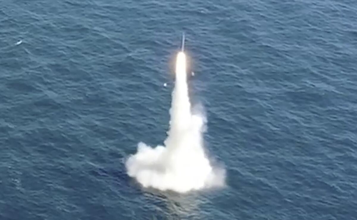 A missile emerges in a plume of white smoke from blue ocean waters