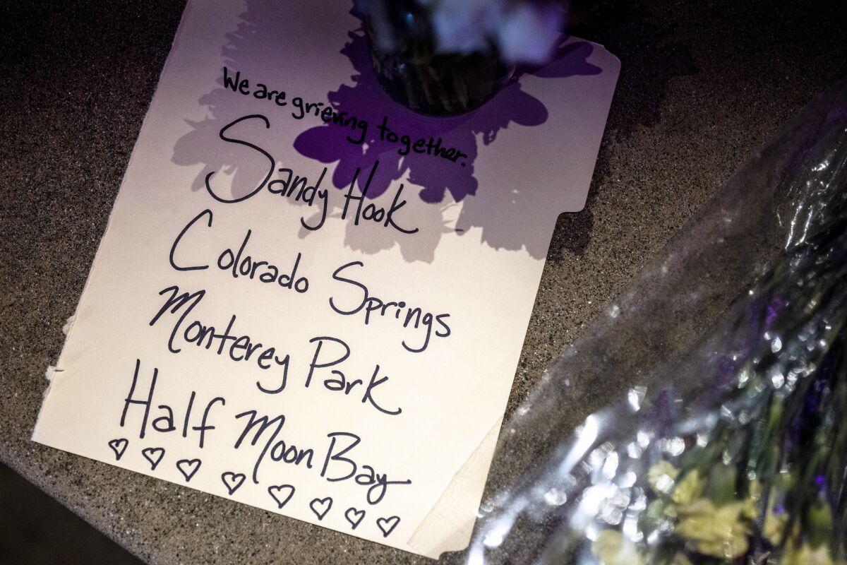 A note laying on pavement reads "We are grieving together. Sandy Hook. Colorado Springs. Monterey Park. Half Moon Bay."